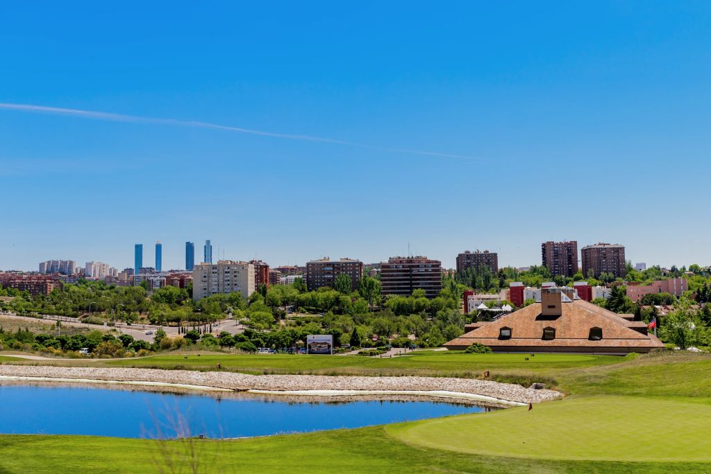 Green and lake at Centro Nacional de Golf with the Madrid skyline behind, on a golf trip to Madrid