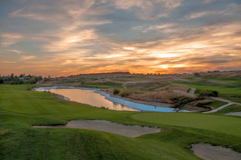 Sunset over Centro Nacional de Golf in Madrid, with clouds breaking over a lake and the fairway