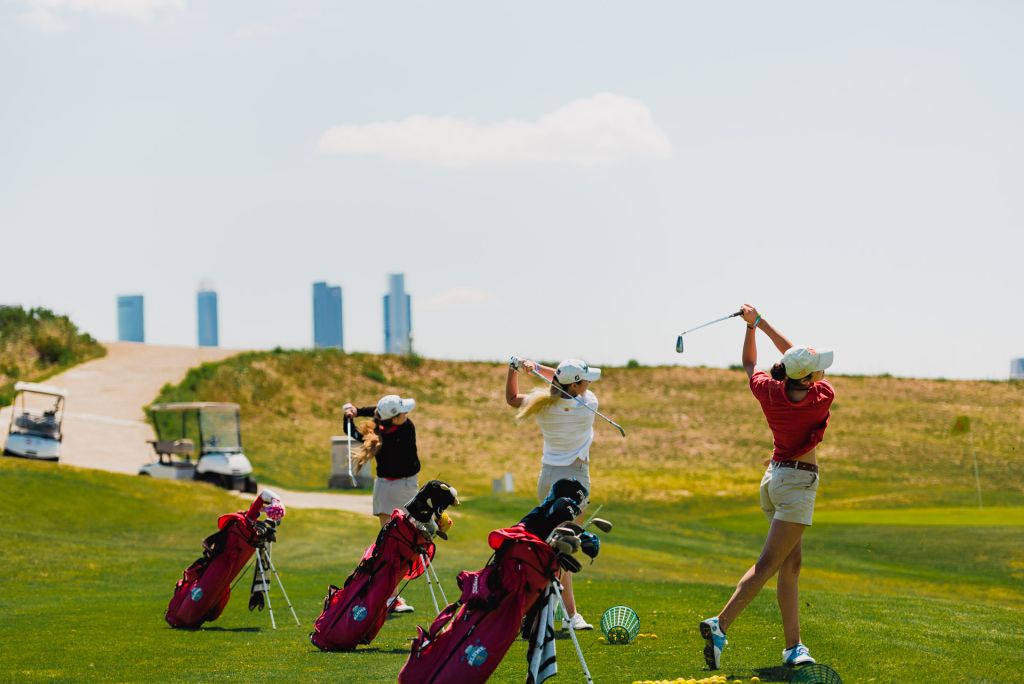 Three golf bags standing beside players on a Madrid golf course with the city skyline on the horizon
